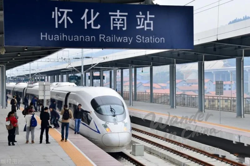 中規模の中国都市にある典型的な都市間バスターミナルの外観写真。駐車中のバスと旅行者の流れを捉えています。日中の自然光の下でシーンを撮影し、駅舎とバスの実用的で機能的な外観を示します。ドキュメンタリー写真のように、地に足の着いた観察的な雰囲気にする必要があります。