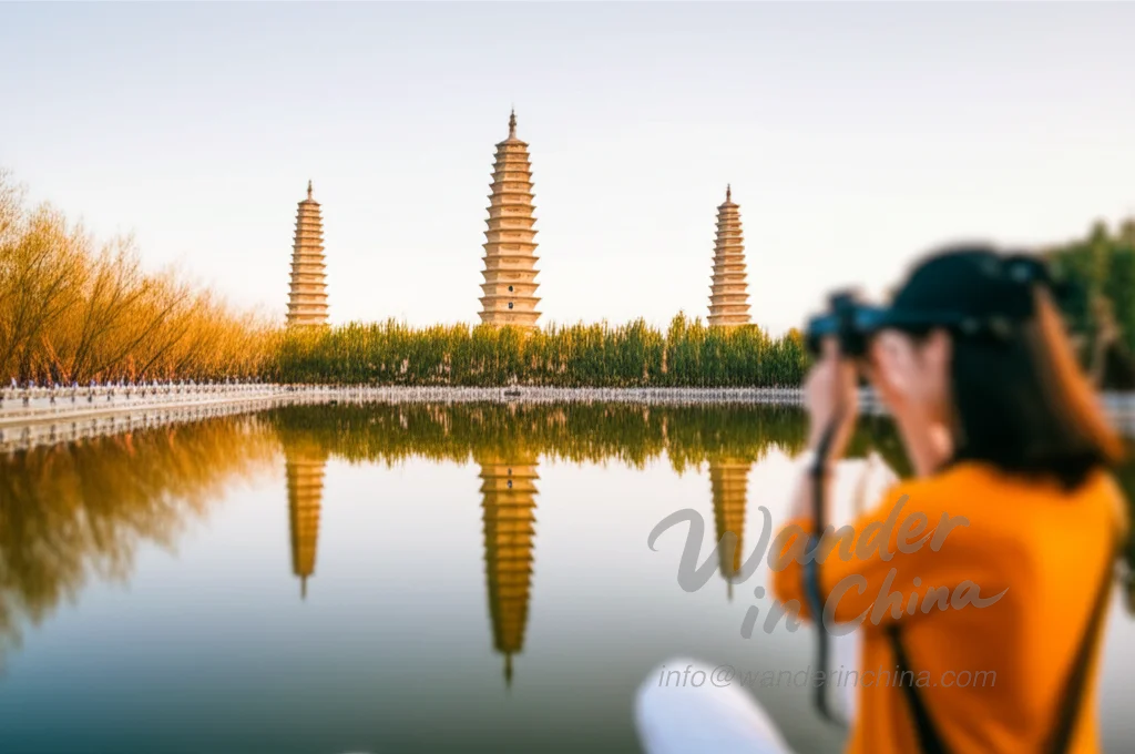 Three Pagodas of Dali reflected in the Reflection Pond with a tourist taking a photo.